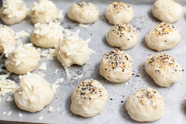 Stuffed Bagel Bites from thelittlekitchen.net stuffed bagel bites with toppings (shredded asiago , everything bagel seasoning) on a parchment paper lined baking sheet