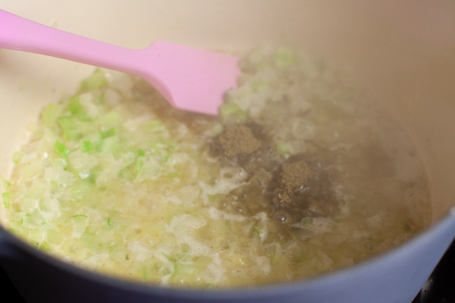 Cooking onion and celery with butter in a pot with a pink rubber spatula